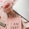 overhead shot of an Apple laptop, pink flowers, mini lightbulbs, markers, and a pink notebook or planner