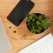 desk with a cell phone, plant, keyboard, notebook and mroe